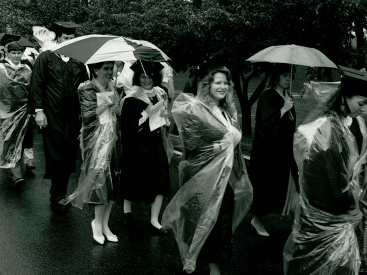 Students process to Commencement holding umbrellas in the rain