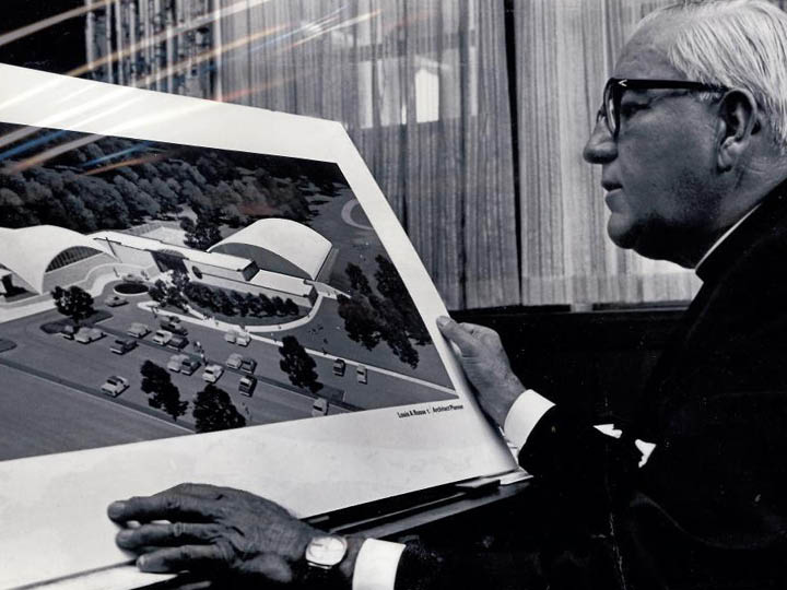 Father Lavery looks at a rendering of the future athletic complex, 1970s
