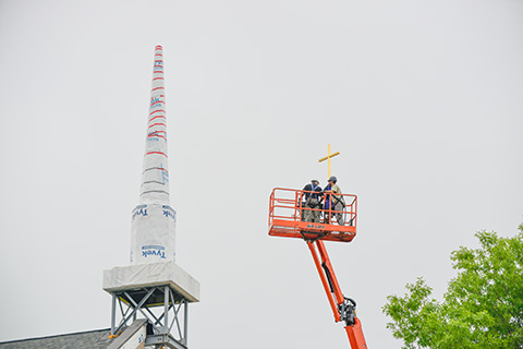 Workers on a lift installing the gold cross on the steeple of the chapel.