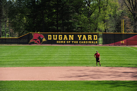 A baseball player in the field at Dugan Yard with banner in the background with text 