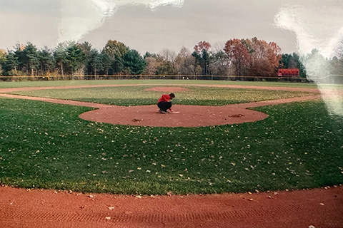 A baseball play kneels at the home plat of Dugan Yard baseball field at Fisher.