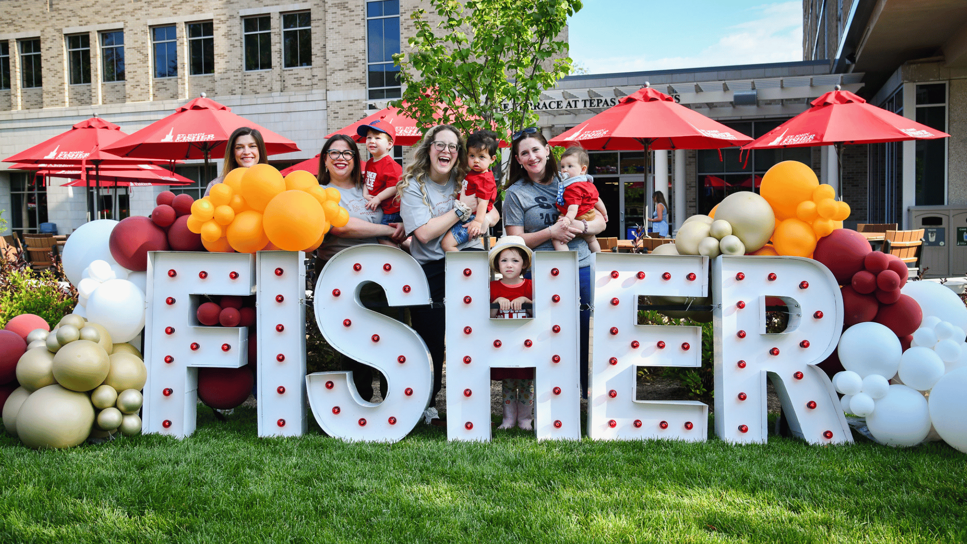 A group of adults and children standing behind Fisher letters