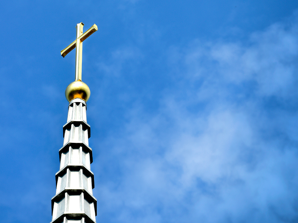 Cross atop a spire with a blue sky background