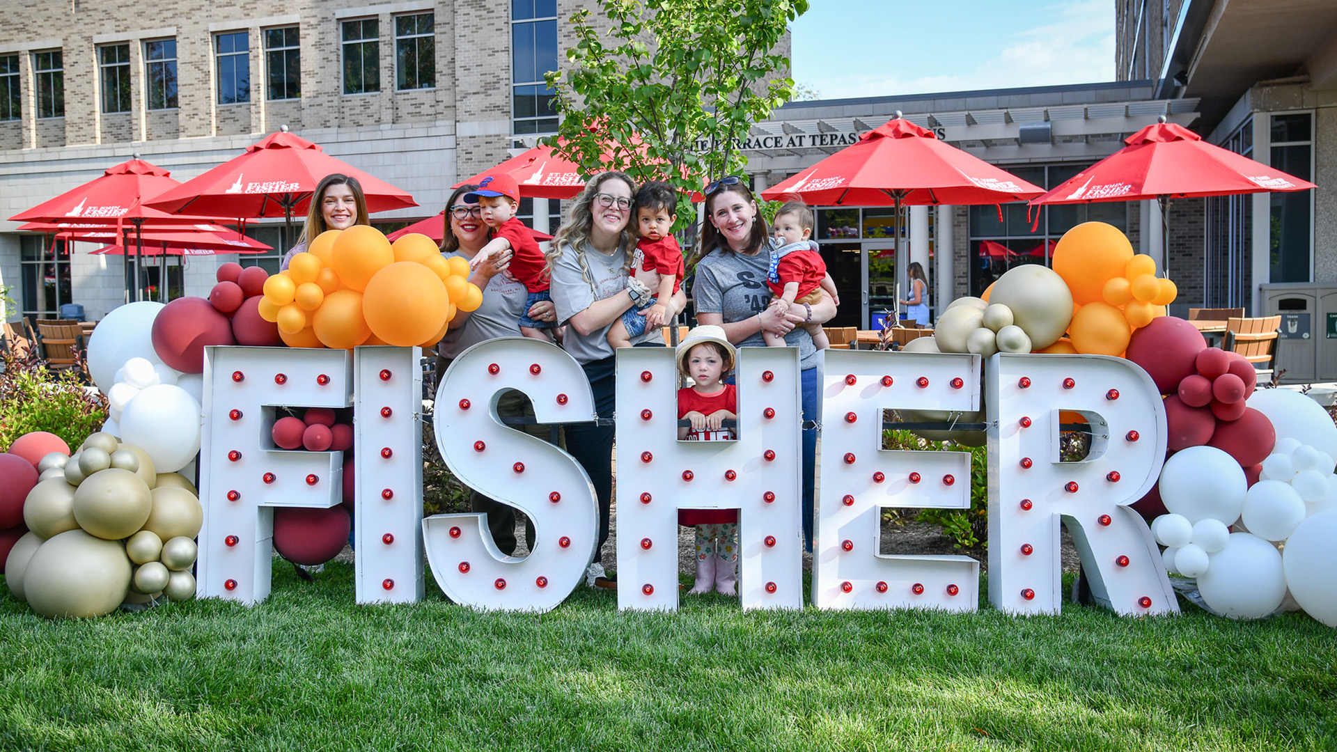 A group of adults and children standing behind Fisher letters.