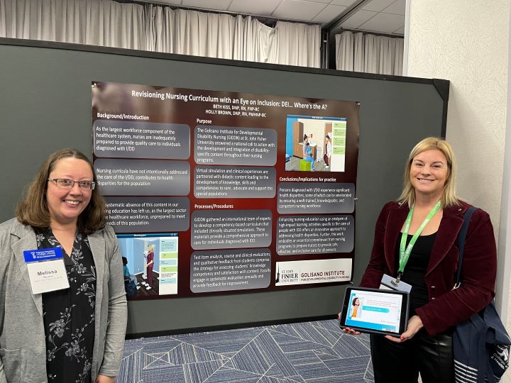Two women standing in front of a poster at a conference.