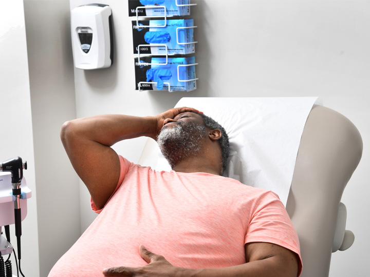 A man in a pink shirt with his hand on his head. He is in a medical setting.