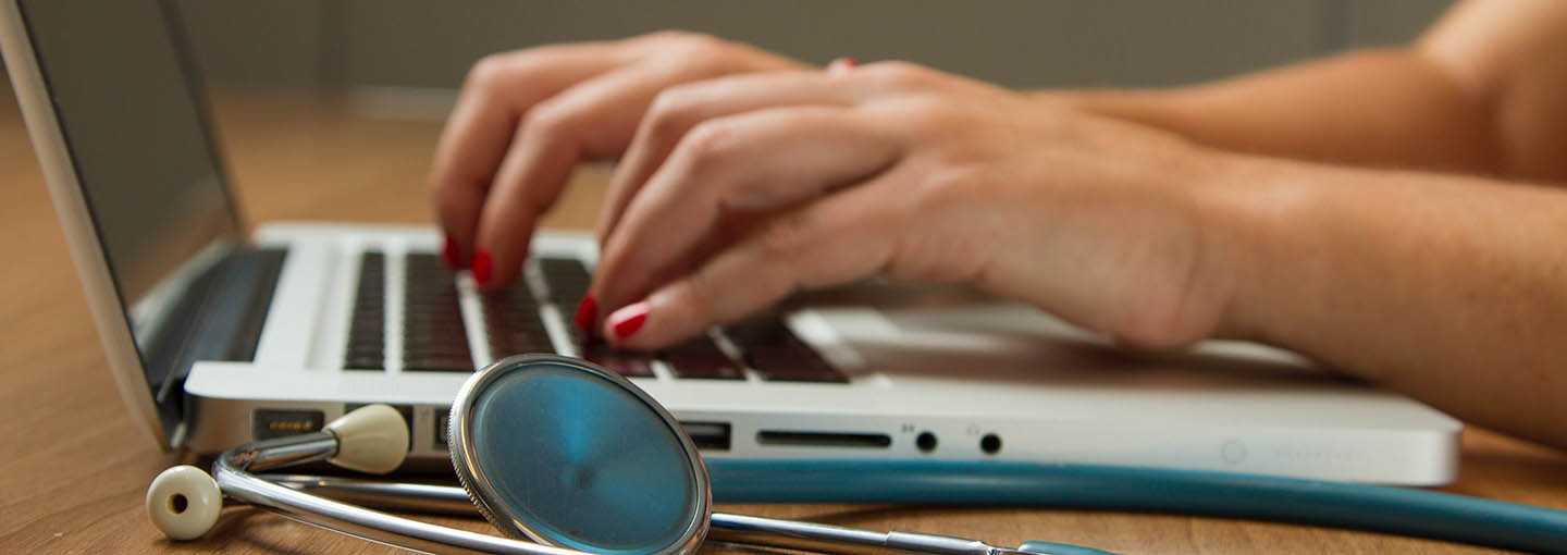 Hands on a laptop next to a stethoscope.