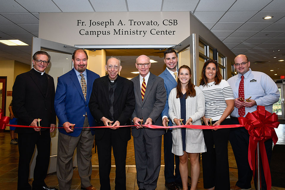 Fr. Kevin Mannara, Peter Mendick, Fr. Joe Trovato, President Rooney, CJ Wild, Maria Wild, Sarah Mancini-Goebert, and Jon Schott help dedicate the newly named Campus Ministry Center.