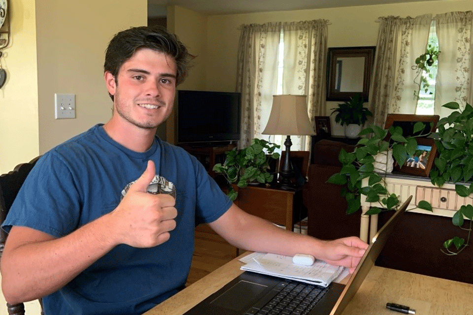 Jacob Vinch gives a thumbs up while sitting at his laptop in his living room.
