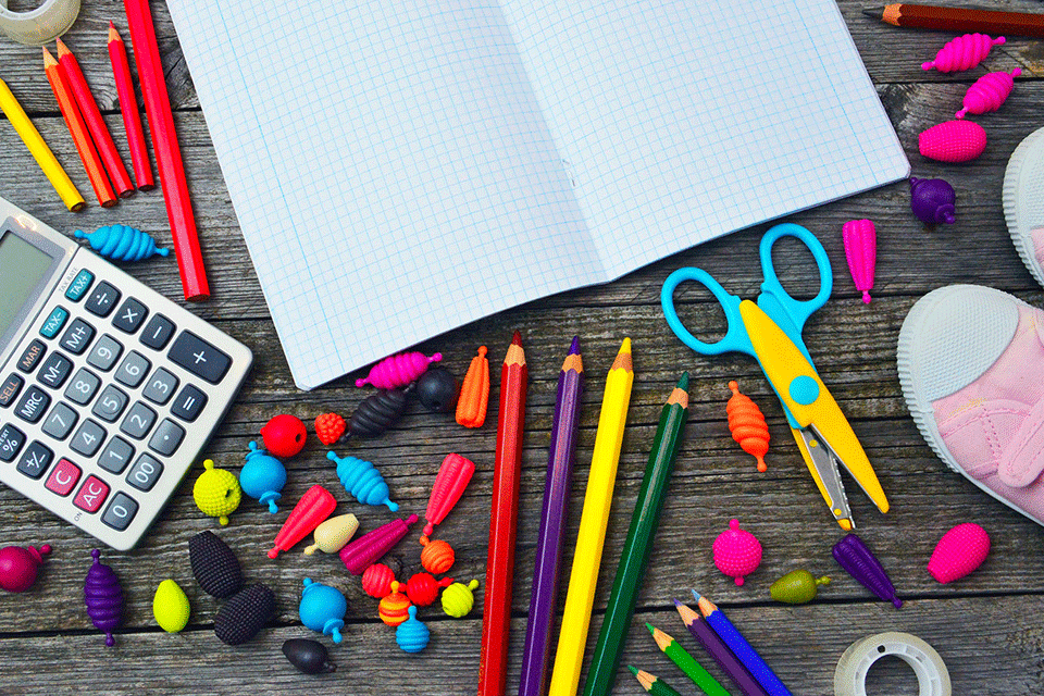 A pile of school supplies, including an open notebook, pencils, scissors, and erasers.