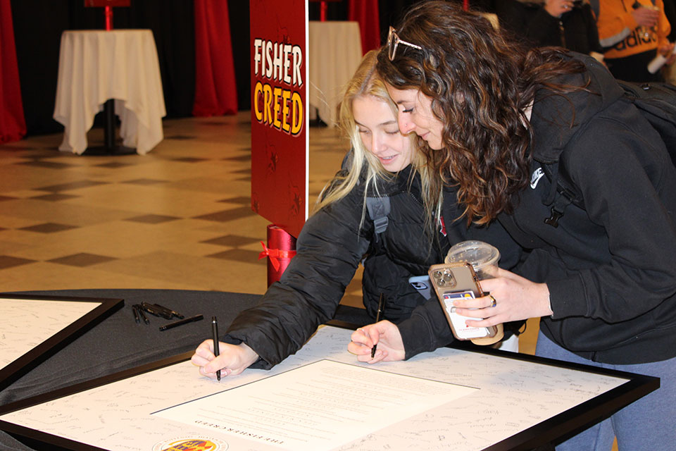 Two students sign the Fisher Creed.