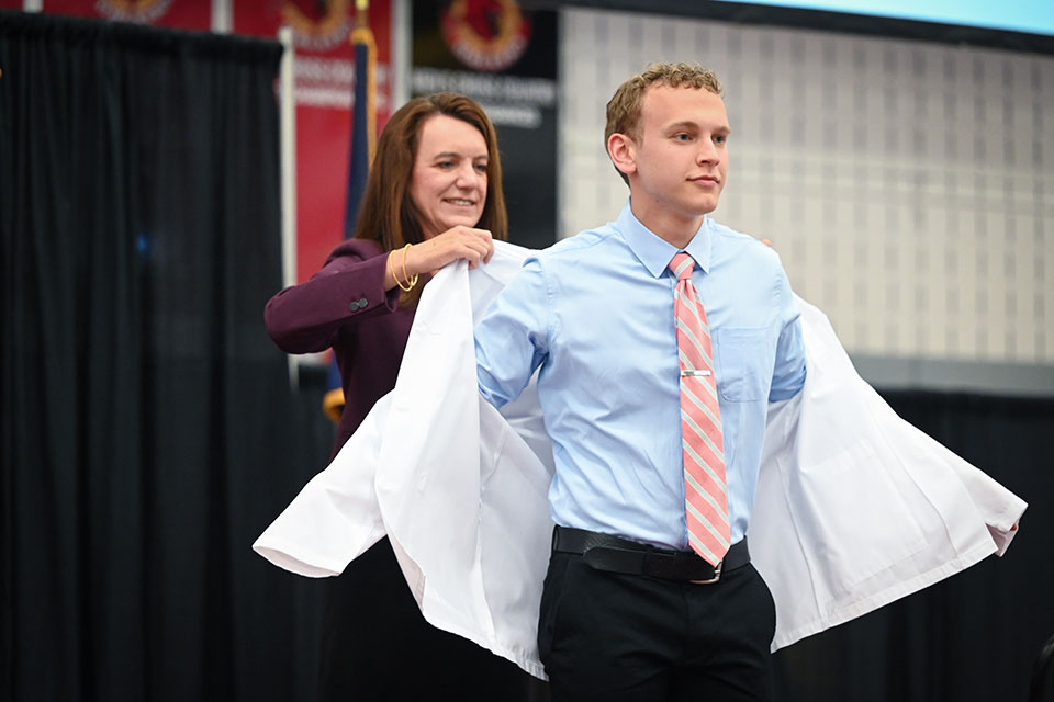 Dean Christine Birnie helps a student into their white coat.