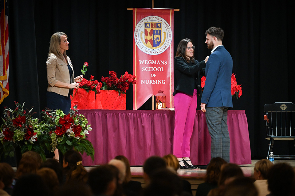 A nursing student receives a pin on stage with a Wegmans School of Nursing backdrop.