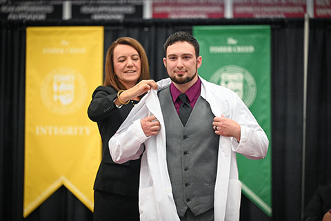 Dean Christine Birnie helps a student into a white coat.