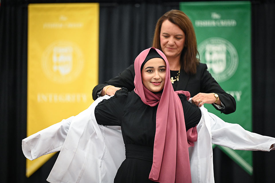 Dean Christine Birnie helps a student into a white coat.