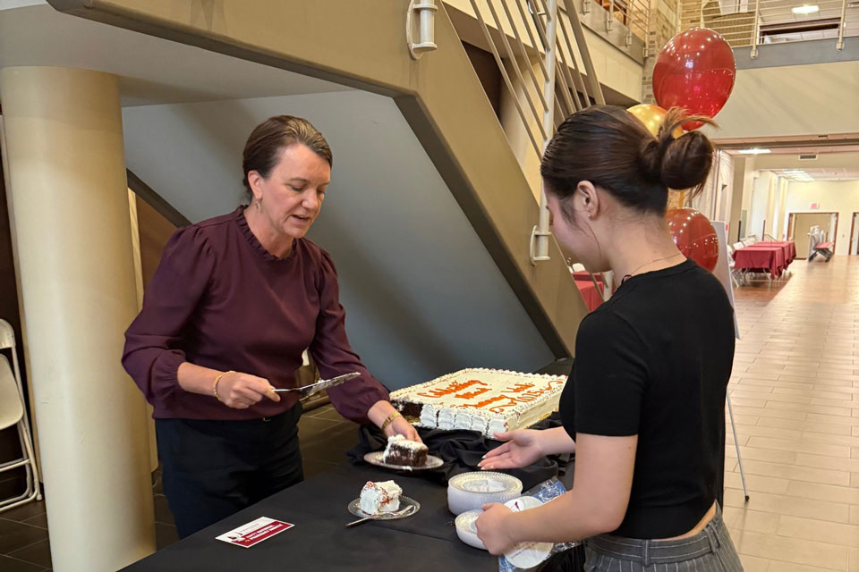 Dean Christine Birnie hands a slice of cake to a student during a Pharmacy Month celebration.