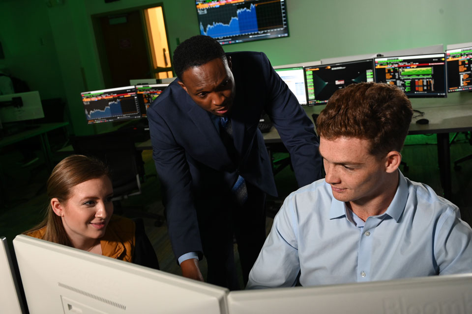 Two students talk with a faculty member during a business class.