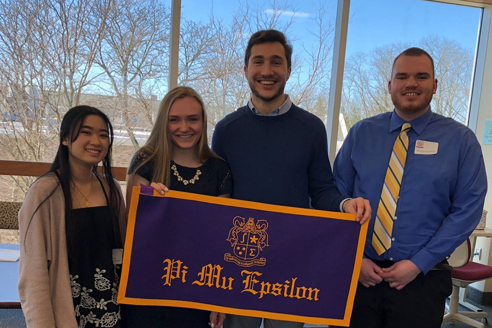 Matina Chanthavongsay, Emily Strong, Charles Petruzelli, and Nicholas Videtti hold a Pi Mu Epsilon banner