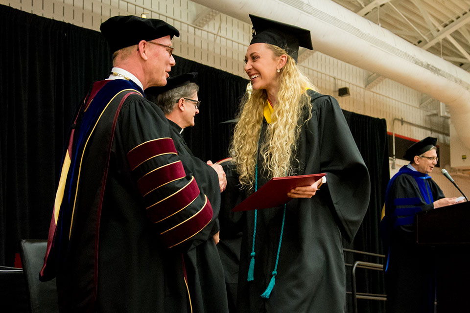 A student shakes hands with President Rooney after receiving her diploma.