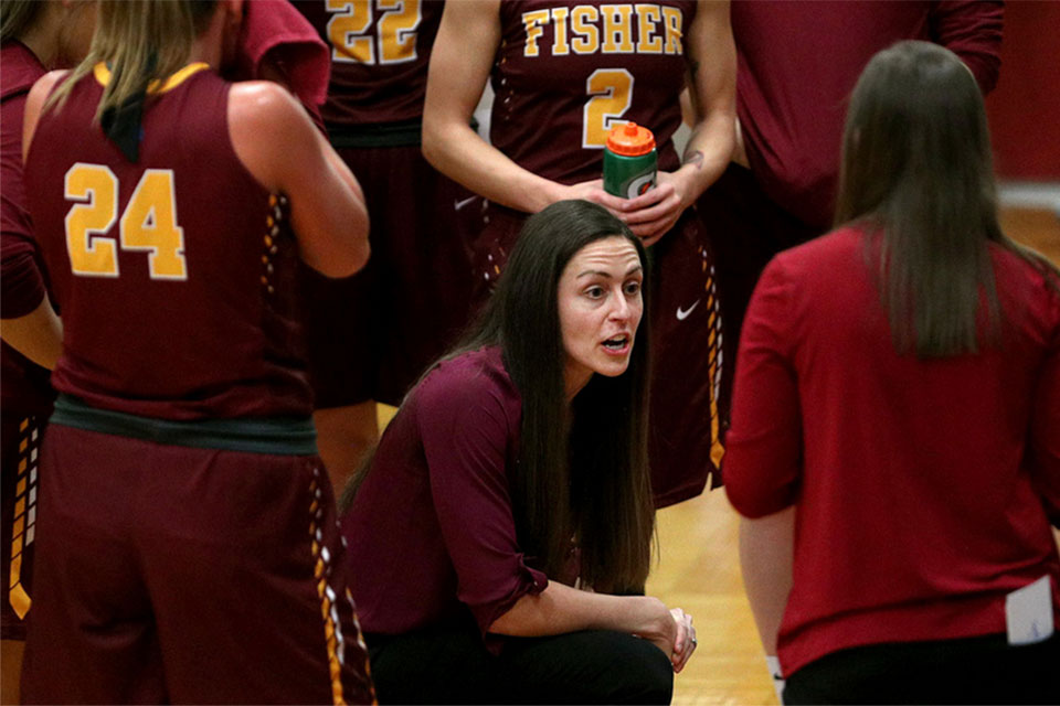 Coach Melissa Kuberka huddles with her team during a women's basketball game.