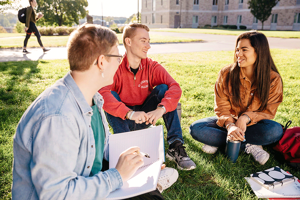 Three students sit and chat on the Quad.