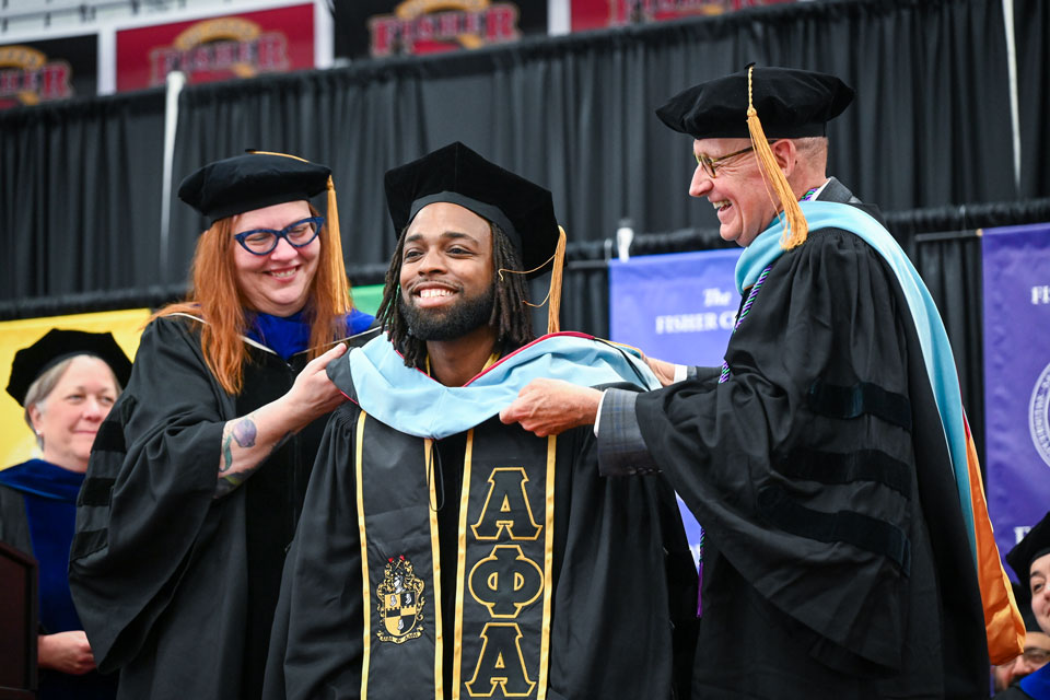 An Ed.D. graduate is hooded by Dr. Maples.