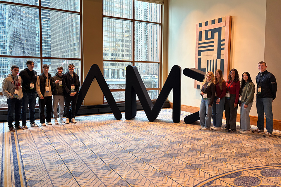 A group of Fisher students of the American Marketing Association stand near the AMA initials.