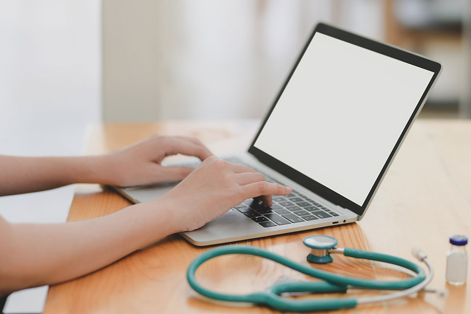 A medical professional types on a laptop.