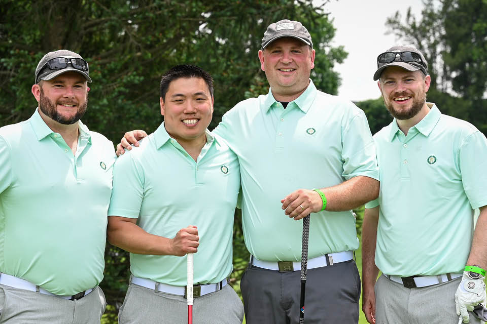 Four men standing together holding golf clubs on golf course