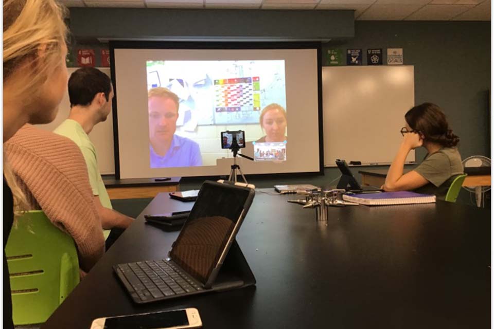 Students working on iPads in a classroom and interacting with other students on the screen.