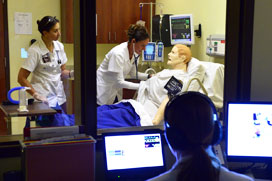 Students working in the Simulation Center facilitated by an instructor in the control room.