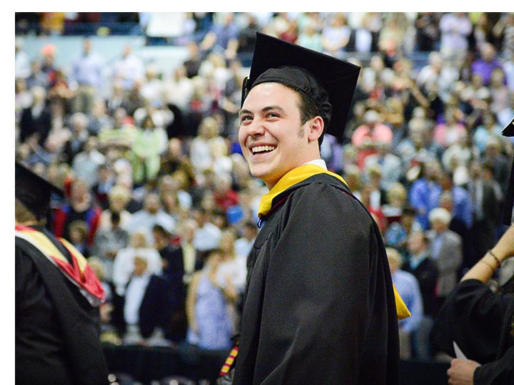 Male student smiles as he enters a packed arena for Commencement.