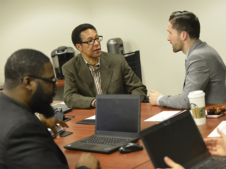 A small group of students have a discussion at a table with laptops