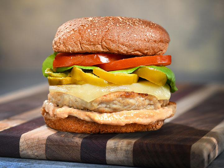 Fisher is home of Turkey Burger Time. Image shows a turkey burger topped with peppers, lettuce, tomato, and cheese on a bun.