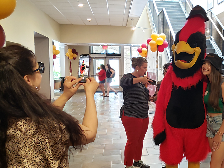 An incoming student poses for a photo with Cardinal, who is wearing a stylish hat.