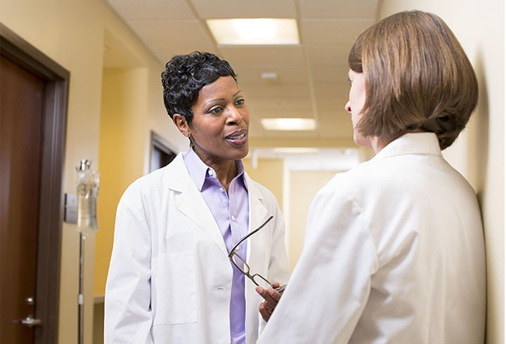 Two nurses in white coats talking in a hallway