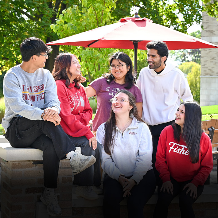 Fisher students sit on campus together with smiles.