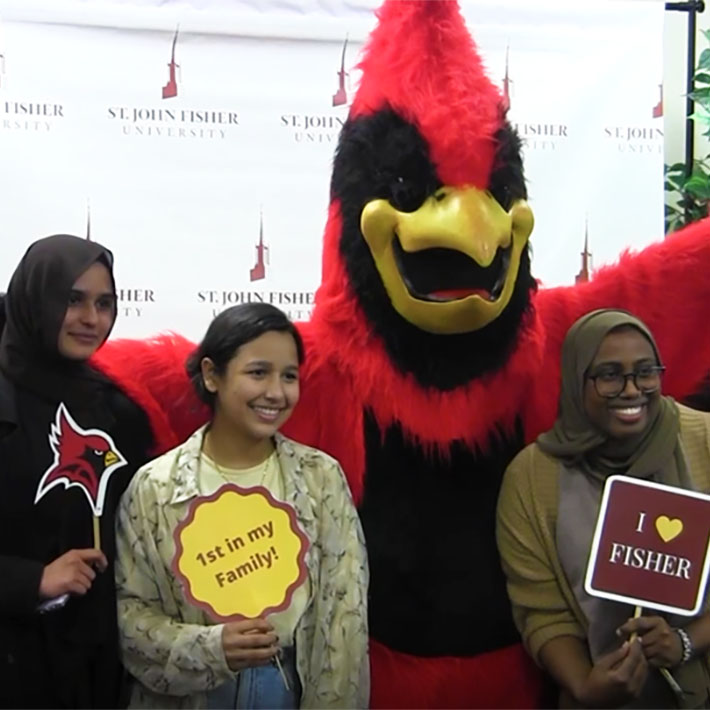 Students stand with the Cardinal mascot and hold signs that read first in my family and I love Fisher.