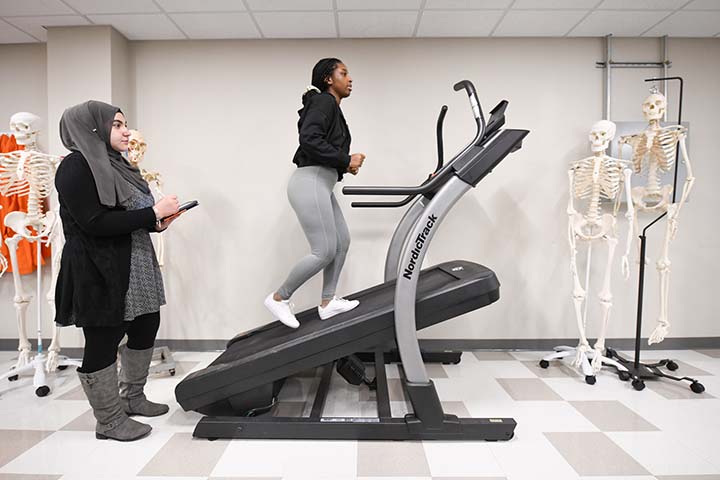 A student takes notes about another student exercising on a treadmill as part of the athletic performance program.