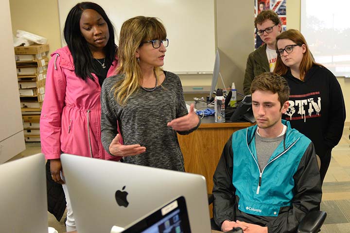 Students standing and seated around a computer in a computer lab.