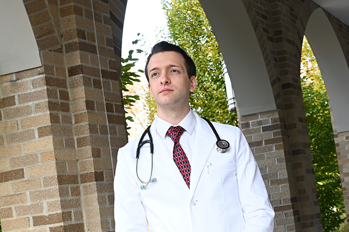 Graduate nursing student stands near the Wegmans School of Nursing with a stethoscope.