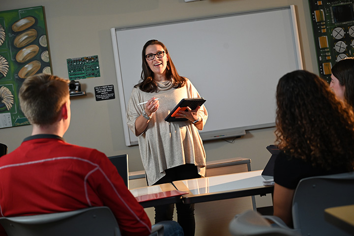 A graduate education student stands in front of a classroom with her iPad in hand.