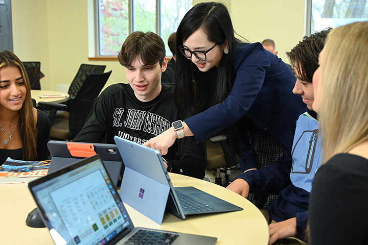 A professor points to an iPad while working with a student in a classroom.