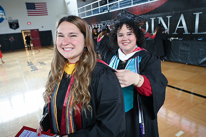 Students in commencement regalia help fix each others robes.