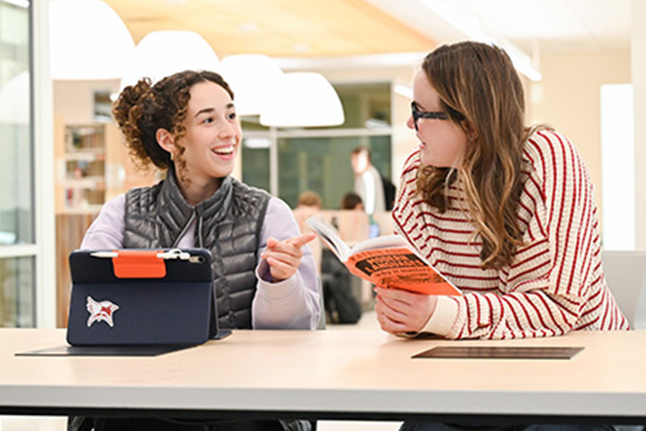 Students chat in Lavery Library over an iPad and a book about modern languages.