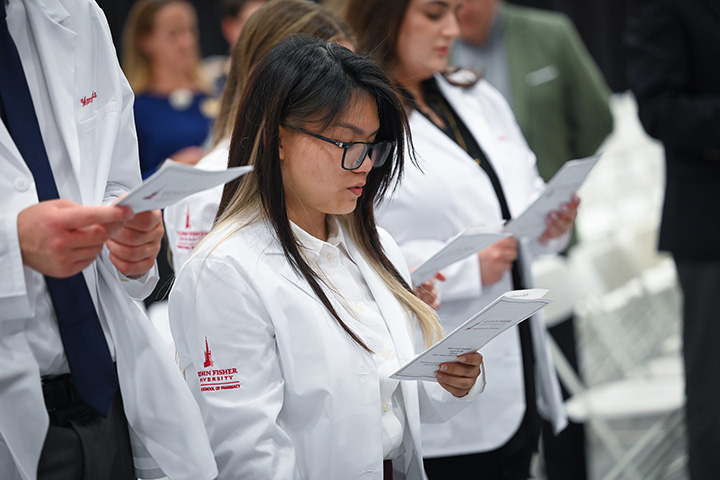 Pharmacy students in white coats taking the oath of a pharmacist.