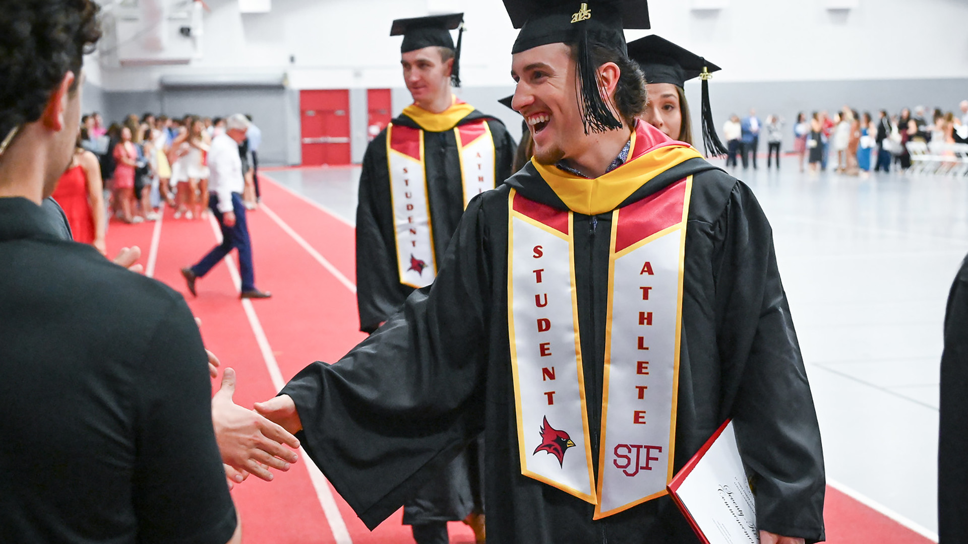 A student athlete in commencement regalia shakes hands in the audience.