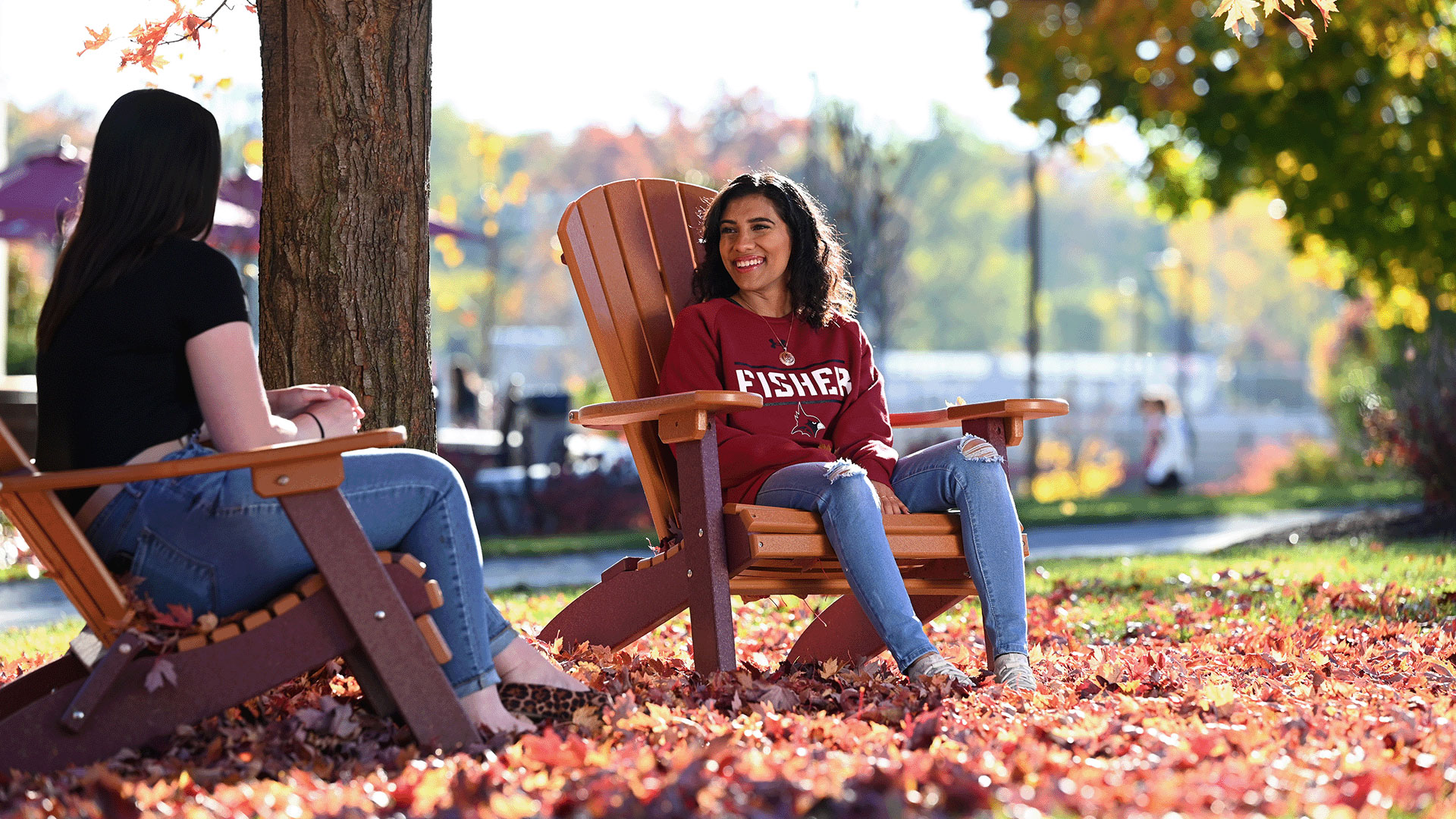 Students sit in Adirondack chairs in the leaves on campus.