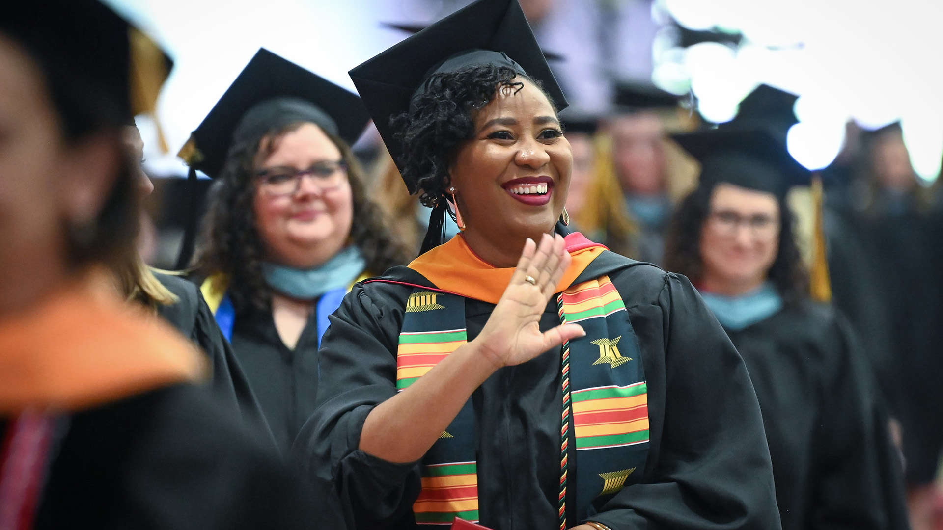 A graduate in commencement regalia waves.