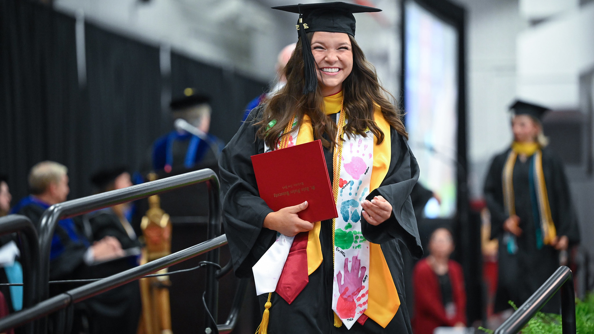 A graduate in commencement regalia with a big grin.
